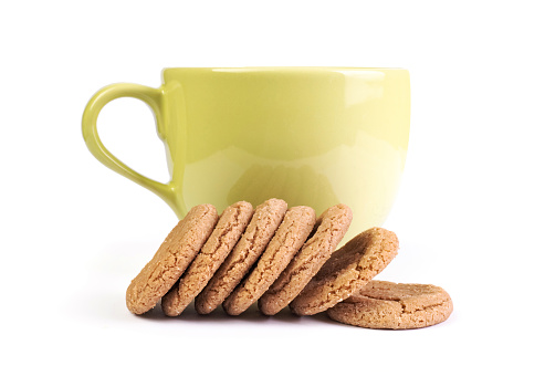 Brown biscuit in front of a large green coffee cup on white