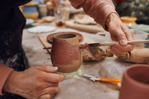 istock Applying engobe on a ceramic mug with a brush in a pottery workshop. Hands close up 1297249941