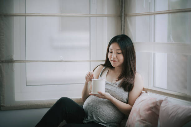 asian chinese pregnancy woman sitting on day time bed relaxing with a cup of tea enjoying - love growth time of day cheerful imagens e fotografias de stock