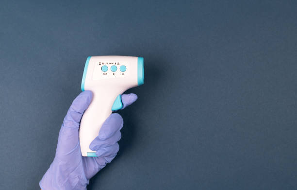 istock Hand in glove holding ir thermometer on dark blue background. Anti virus protect concept. Medical office measurement product. Healthcare home action. Distant temperature check 1297253473