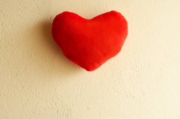 istock Red plush heart hanging on a yellow wall 1297253525