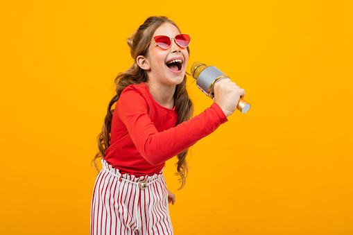 young singer with a microphone in her hands on a yellow studio background with copy space.