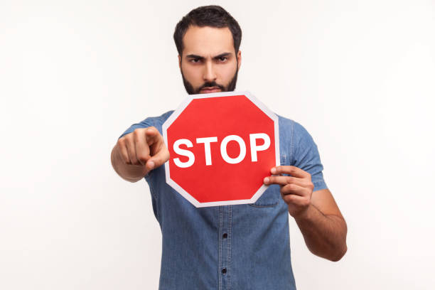 istock Strict angry man with beard holding stop sign and pointing at camera with serious face expression, control, security 1297255395