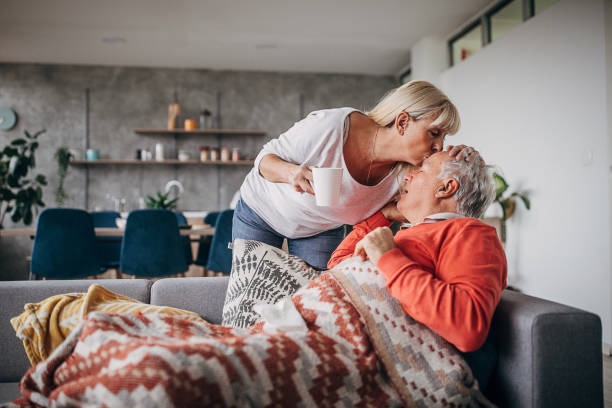 Woman kissing her husband on forehead who is ill with flu Man and woman, senior couple at home, woman kissing her husband on forehead who is ill with flu. cold and flu man stock pictures, royalty-free photos & images