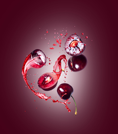 Whole and sliced sweet cherries with splashes of juice on a red background