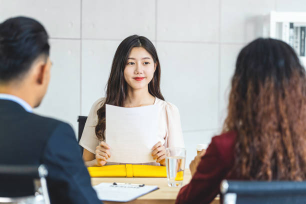 若いアジアの女性卒業生は、履歴書を保持し、会議室で肯定的な動きで就職面接を開始する前に2人のマネージャーに準備し、ビジネス採用新会員の概念 - 就職面接 ストックフォトと画像