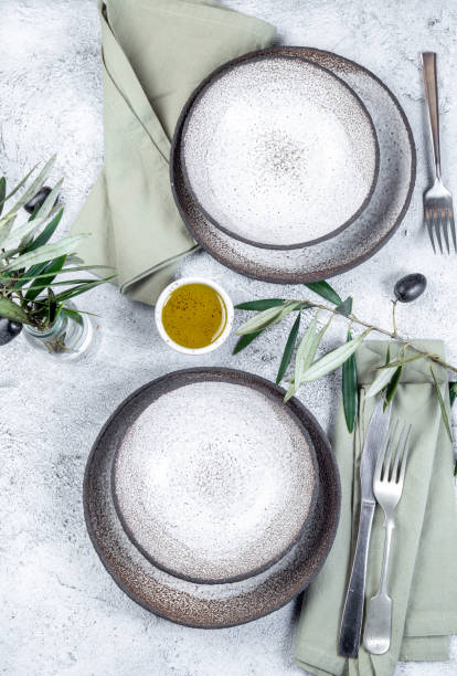 istock Mediterranean set table. Gray plates, forks, green napkins and olive tree branches 1297268690