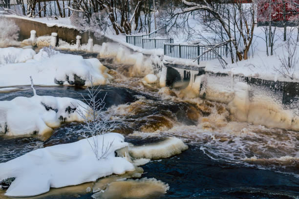 Winter forest on the river at sunset. Colorful landscape with snowy trees, beautiful frozen river with reflection in water. Seasonal. Winter trees, lake and blue sky. Frosty snowy river. Weather