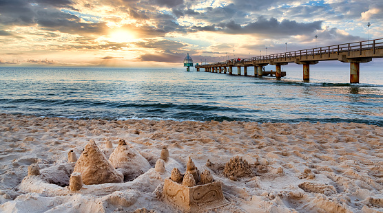 Pier and beach with sand castles in foreground in Zinnowitz at sunset. Baltic Sea, island Usedom, Germany
