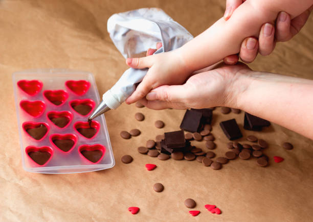 family cooking class. mommy and me handmade valentines day dessert. making chocolate candy,kids hands filling hearts - chocolate chocolate candy dark chocolate pouring imagens e fotografias de stock