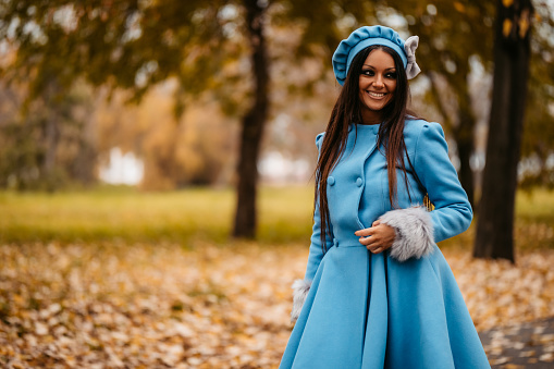 Elegant beautiful young woman walking in autumn public park wearing coat.