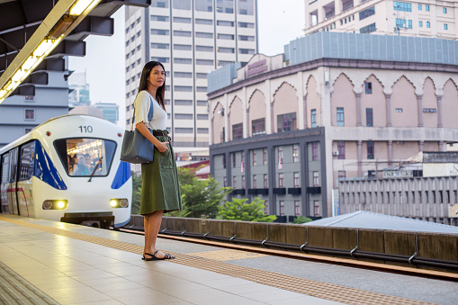 MRT or subway train is approaching the Central Market station in Kuala Lumpur, and Asian woman waiting on railway platform