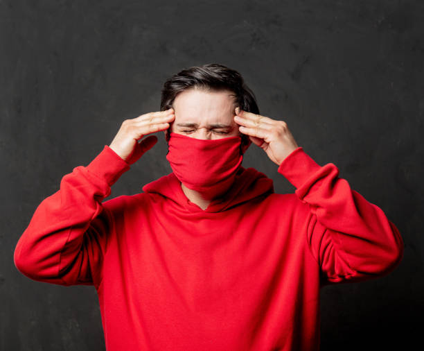 istock guy in red sweatshirt and face mask with headache on dark background 1297280468