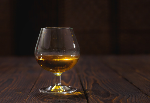 Glass of whiskey or brandy on wooden table on dark abstract background.