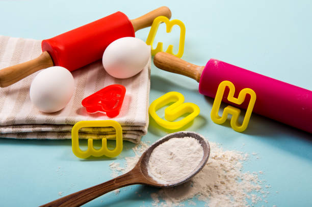 istock Cooking class for kids concept. Eggs, flour, rolling pins, letter shape cookie cutters on light blue background, studio shot. 1297282734