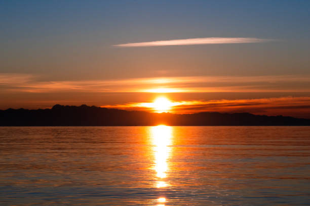 Landscape picture of the midnight sun over the polar circle in Norway during the longest days during summer. Red sun touching the sea between small islands on norwegian coast of north atlantic ocean.
