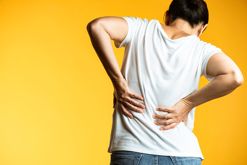 Back of unrecognizable female who is holding her belly with her two hands because of back pain.