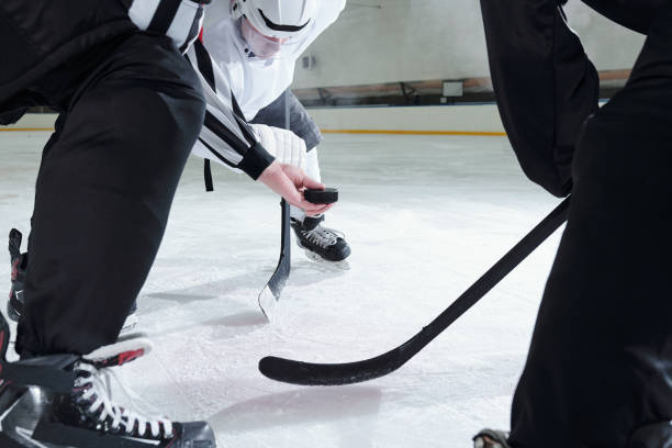 istock Hockey referee holding puck over ice rink while two rivals with sticks around 1297286069