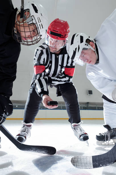 istock Hockey referee holding puck over ice rink while rivals with sticks looking at it 1297286081