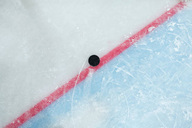 puck deitado na linha vermelha dividindo espaço de jogo e zona de rede em grande pista de gelo - ice rink ice hockey ice playing - fotografias e filmes do acervo