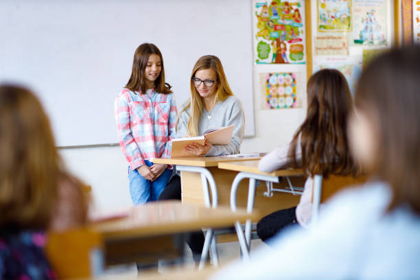 istock Happy elementary girl talking to her teacher on a class in the classroom 1297286422