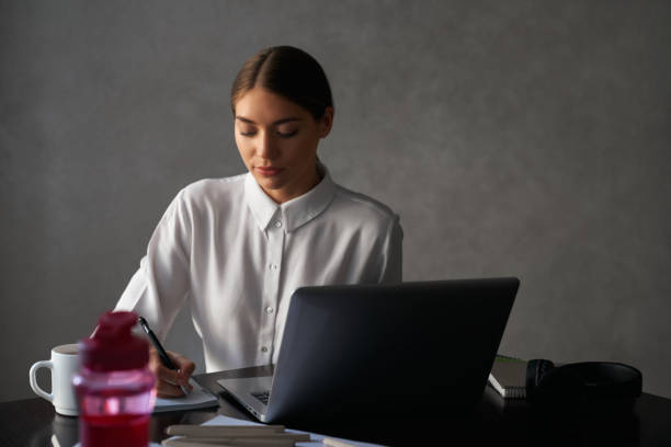 istock Woman sitting at table with laptop and writing notes 1297287859