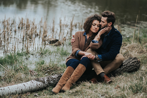 caucasian couple in love in autumn nature. Young bearded man and curly woman are hugging on the shore of a lake