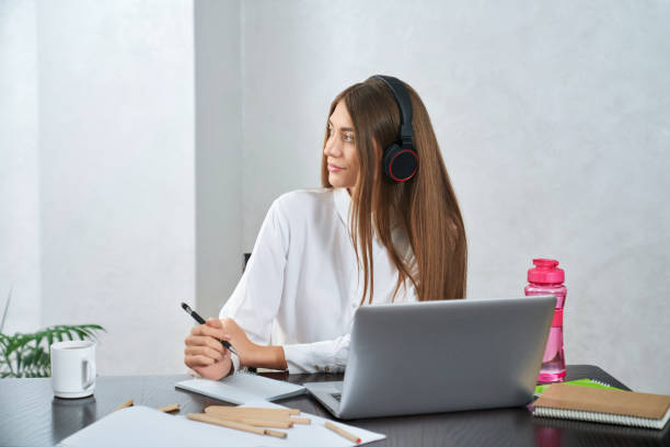 istock Pretty student in headphone sitting at table with laptop 1297288600