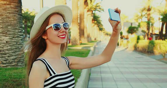 Portrait of smiling woman taking selfie picture by smartphone on a palm tree background