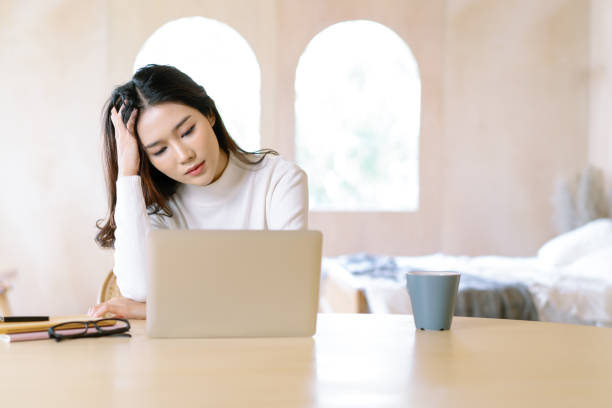 istock Freelance stress. Tired exhausted young beautiful Asian woman freelancer about problem with laptop, having problems with project,feeling depression,lazy during at home office desk in winter holiday. 1297290957