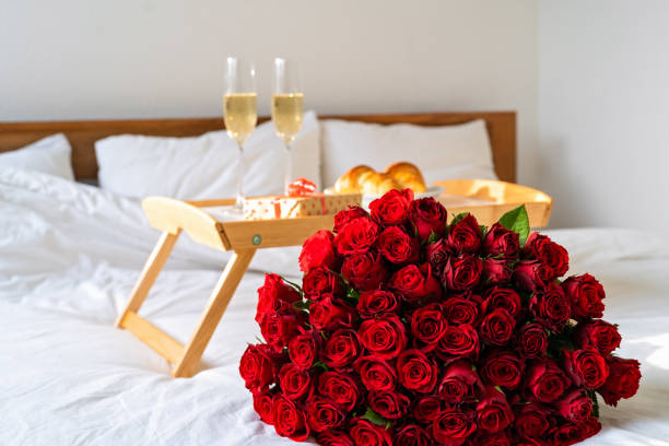 Celebrating Saint Valentine's Day with bouquet of red roses, glass of champagne and croissants on tray on bed. Romantic surprise breakfast for Mother's day or International women day stock photo