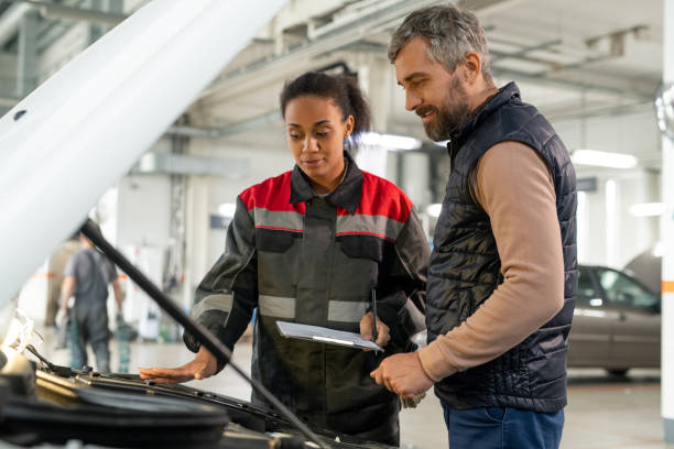 istock Young female technician of car repair service looking at open engine compartment 1297291893