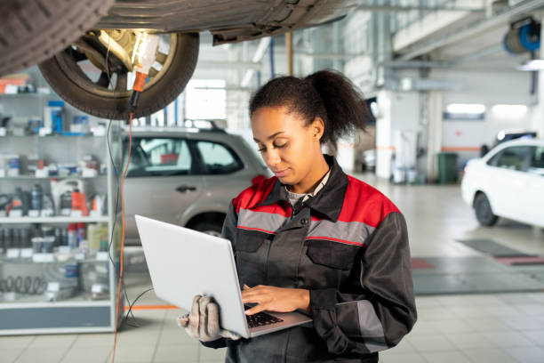 Female worker of car maintenance service in uniform using laptop in workshop