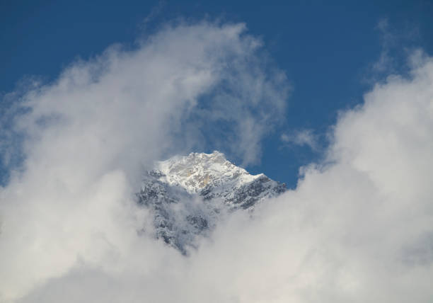Snow covered mountain peak with summit cross peeking through clouds