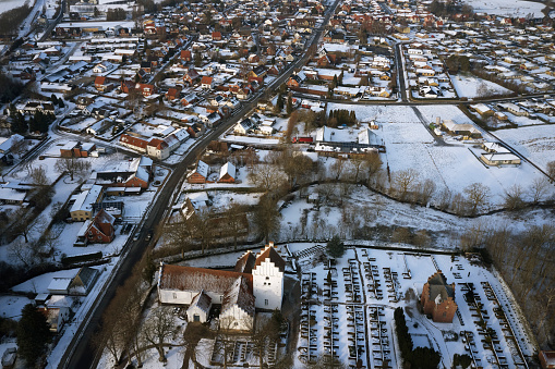Local small town in Denmark. Winter and snow on the roof tops. Traditional Danish village church. Drone shot