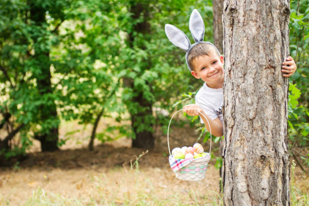 criança feliz olha para fora de uma árvore segurando cesta cheia de ovos de páscoa coloridos após a caça ao ovo na primavera. feliz dia de páscoa. - face paint child paint rabbit - fotografias e filmes do acervo