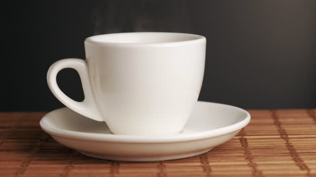 Hot water is poured into a white ceramic cup. On the table is a bamboo mat.