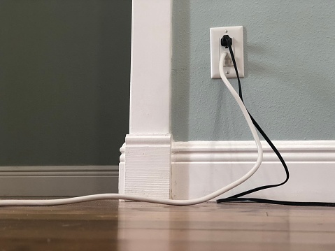 Low angle view of hardwood floor and complementary wall color and white molding with hazardous placement of electrical cords