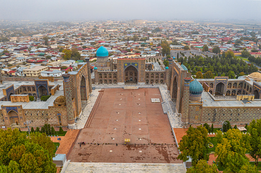 Aerial view of the world famous Registan Square in the city of Samarkand. The buildings were build from King Timur Tamerlan in the 14th century when the city of Samarkand became the capital of the Timurid Empire. The full ensemble of the Registan Square is listed as UNESCO World Heritage Site. Samarkand was one of the most important oasis and place of caravanserais at the Great Silk Road.