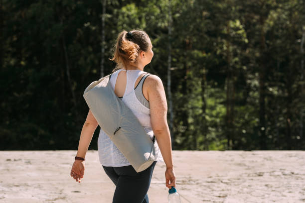Getting Away from the City: Anonymous Plus Size Woman Walking in the Mountain and Carrying her Yoga Mat An unrecognizable plus size woman wandering in nature, carrying her yoga mat. splash mountain stock pictures, royalty-free photos & images