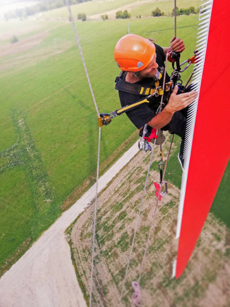 istock Blade repair: High angle view on Industrial climber,  rope access technician working on gigantic onshore wind-turbine blade and inspecting serration on blade, road and country side under him 1297308944