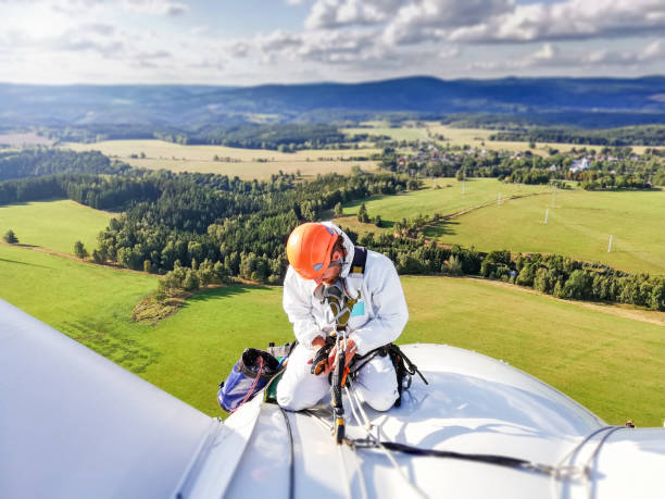 Industrial climber,  rope access technician kneeling on enormous onshore wind-turbine while preparing for blade inspection with amazing view on Ore mountain (Krusne hory) moutain range stock photo