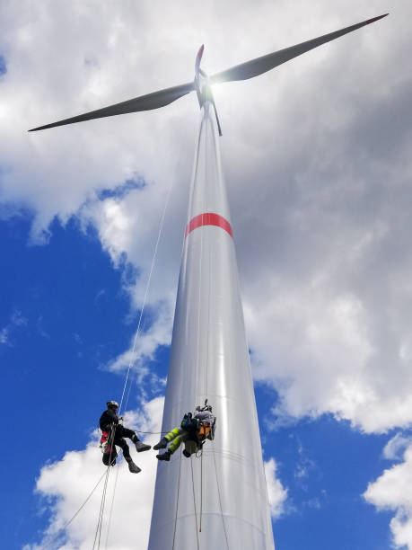 istock View from bottom on wind-turbine and two rope access technicians rappelling down from blade on the ropes, doing inspection, dramatic sky and sunny day. 1297308988