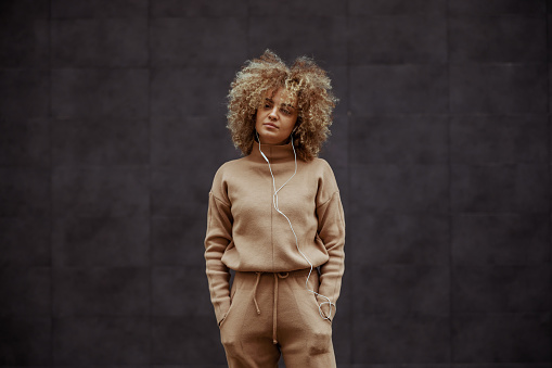Hip hop girl in tracksuit standing with hands in her pockets and listening music.