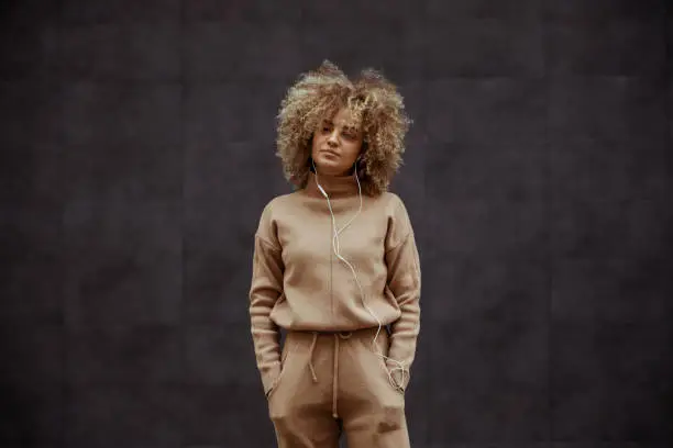 Photo of Hip hop girl in tracksuit standing with hands in her pockets and listening music.