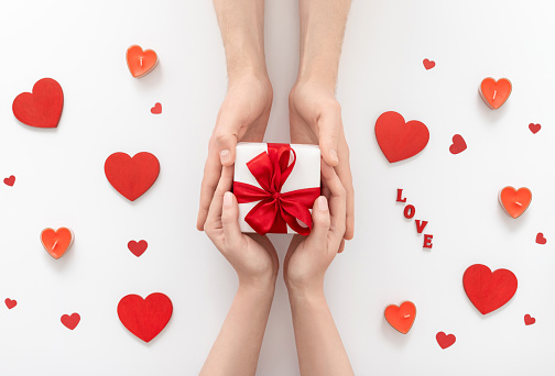 Man and woman hands hold gift box on white background. Love and Valentine's day concept. A man gives a gift to a woman. Top view, flat lay.
