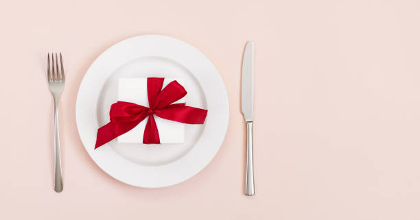 istock Festive table setting with a gift in a plate on a pink background. Banner. Space for text. Top view. Valentines Day, Mothers Day, Birthday or Christmas. 1297320687