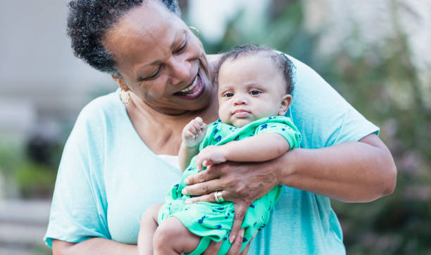 African-American grandmother with baby boy A senior African-American woman in her 60s holding her grandson, a 3 month old baby boy. He is looking at the camera while his grandmother looks down at him proudly. grandmother real people front view head and shoulders stock pictures, royalty-free photos & images