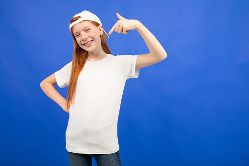 attractive red-haired teenager girl in a white T-shirt with a layout shows the class on a blue studio background.