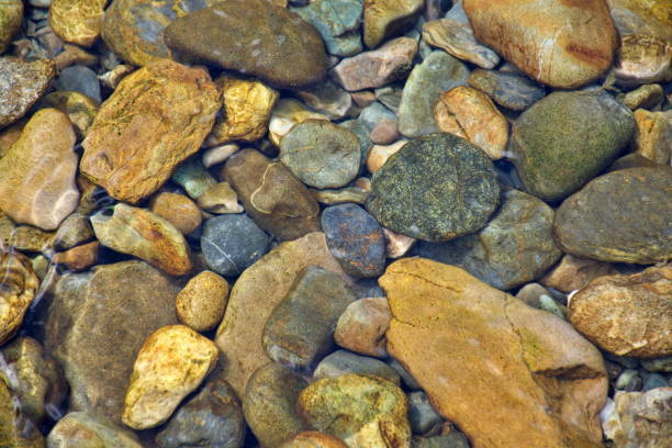 Looking down to river stones through pure fresh clear river water. Riverstone background in full frame.